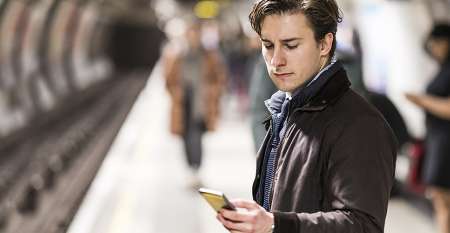 Young person waiting for tube train on platform looking at mobile phone