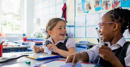 Two girls in classroom looking at each other smiling