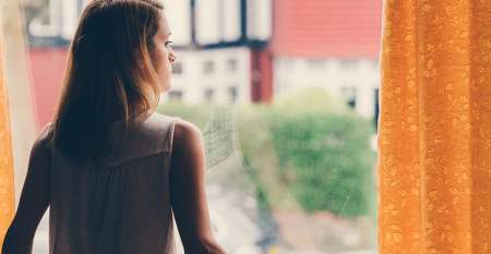 Young woman staring out window thinking about her debts
