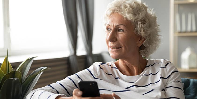 Older woman looking out window using mobile