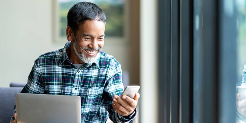 Man with laptop smiling looking at mobile phone.