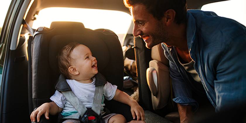 Man leaning over towards baby in car seat as both are smiling