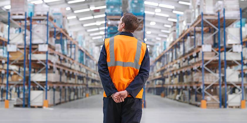 Warehouse worker in orange tunic facing shelving aisles.