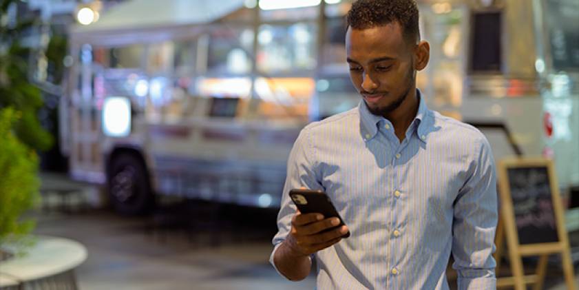 Young man in smart shirt outside at night looking at mobile phone.